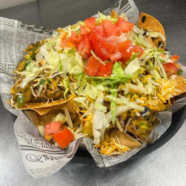 A large serving of Port City Cheesesteak nachos, topped with shredded lettuce, diced tomatoes, and cheese.