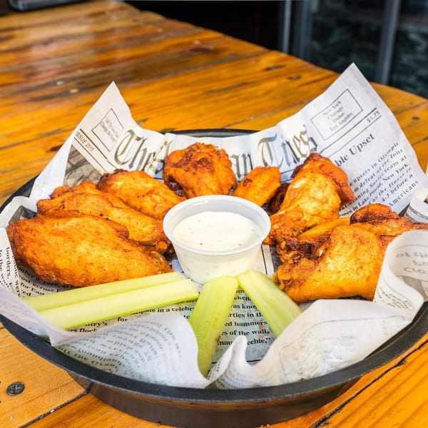 A basket of Port City Cheesesteak's crispy chicken wings with celery sticks and ranch dressing.