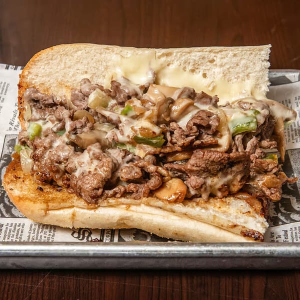 A Port City Cheesesteak with steak, melted cheese, mushrooms, onions, and green peppers on a roll.